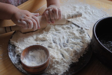 Children's rolling pin for dough. The child kneads the dough with his hands. The baby's hand sifts the flour.
