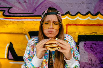 Attractive hungry woman, enjoying eating a burger, closed her eyes. Dressed in stylish jacket and...