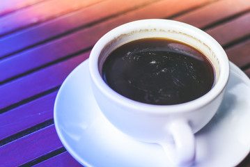 A cup of hot espresso coffee on plate on wooden table in morning rush time with colorful lighting