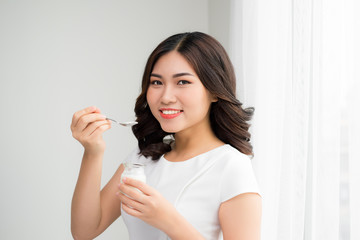 Portrait of young asian woman at home eating yogurt