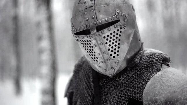 Portrait closeup of militant medieval knight wearing traditional steel armor and helmet, sword fighting in winter wood slow motion. Fantasy and reenactment