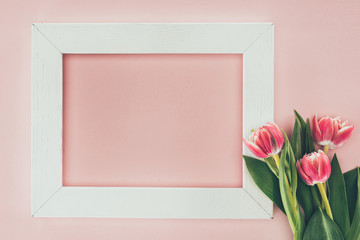 beautiful pink tulips and empty white frame on pink