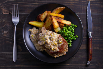 Beef steak with mushroom cream sauce, potato wedges  and green peas. View from above, top