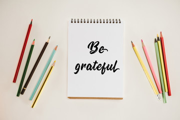 top view of notepad with be grateful lettering and colorful pencils isolated on white
