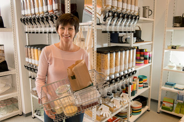 Verpackungsfreies Einkaufen, Frau mit Warenkorb vor Regalen mit unverpackten Produkten
