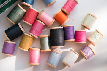 Many multicolored sewing threads on wooden coils are scattered on a white surface