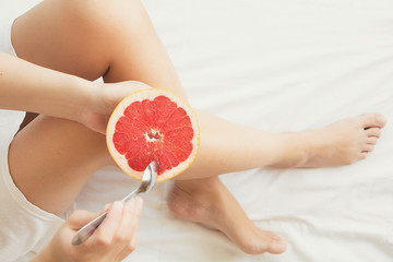 Healthy eating concept. Woman having grapefruit in bed. Top view. Toned