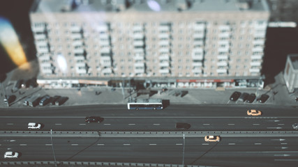 True tilt-shift shooting of highway in metropolis from the high point: residential building, the road in focus with cars, taxies and public transport, crosstown traffic, and street lanterns, sunny day