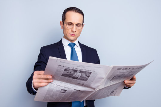 Portrait of focused concentrated strict minded confident respectable proud freelancer having a rest reading the latest news holding newspaper isolated on gray background copy-space
