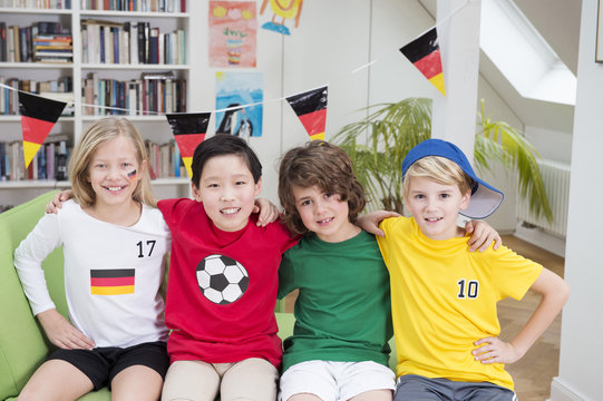 Four children in football shirts sitting on couch with arms around