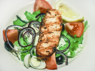 Salad with salmon, tomatoes and quail egg on a white plate