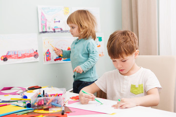 Happy cheerful children drawing  in paper using a lot of painting tools sitting at a table.   
