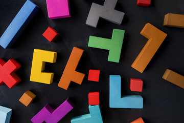 Different colorful shapes wooden blocks on black background, flat lay. Geometric shapes in different colors, top view. Concept of creative, logical thinking or problem solving. Copy space.