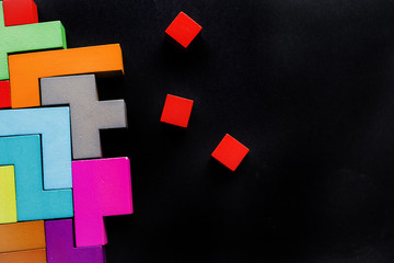 Different colorful shapes wooden blocks on black background, flat lay. Geometric shapes in...