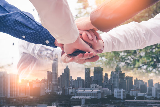 the double exposure image of the many businessmen take a hands together during sunrise overlay with cityscape image. The concept of agreement, business, cooperation, partnership and successful.