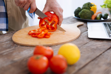 Important nutrients. Close up of appealing strong male hands using knife for rifling bel pepper and...