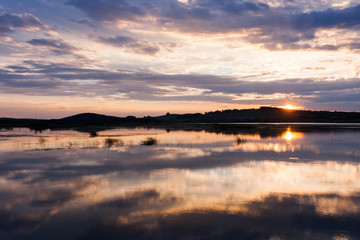 Beautiful summer sunset with cloudy sky and setting sun on the river.