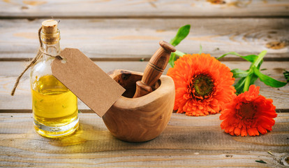 Calendula essential oil and fresh blooming twig in a mortar, wooden table, blank tag, copy space