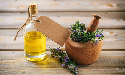 Rosemary essential oil and fresh blooming twig in a mortar, wooden table, blank tag, copy space