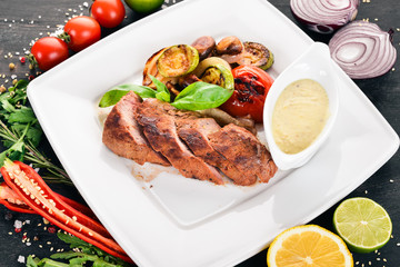 Pork steak with grilled vegetables on a plate. On a wooden background. Top view. Copy space.