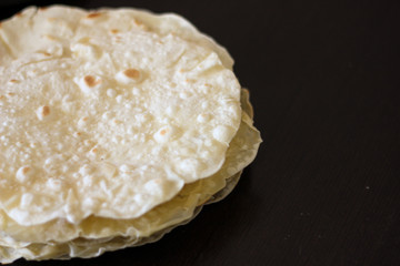 Stack of homemade round tortillas on black table background. Tortilla or pita made of wheat flour, ingredient for cooking burritos, tacos, quesadilla. Flatbread or lavash with space for text
