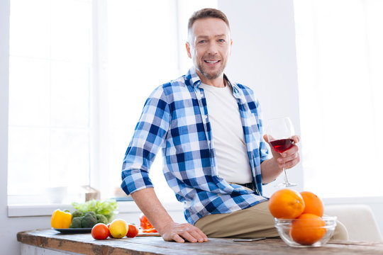 Simple recipes. Pretty happy joyful man drinking wine while staring at camera and grinning