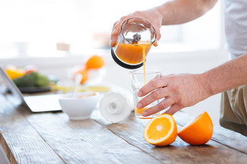 Orange scent. Close up of male hands holding transparent clean glass while spilling orange juice and consuming vitamins