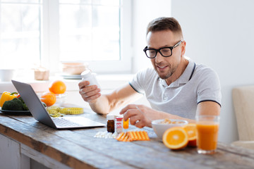 Biohack your brain. Smart skillful thoughtful man searching for biohacking supplements while using laptop and smiling