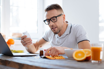 Biohack your life. Handsome progressive doubtful man deciding about biohacking supplements while sitting and improving his health