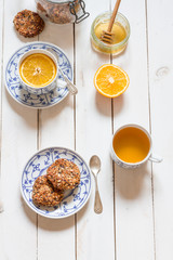 Dates and coconut cookies. Green tea with orange in white and blue cup. White wooden plate. Flatlay.