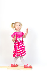Little girl 3 years old in a red dress with bows in her hair. Beautiful girl in a beautiful fluffy dress posing against a white wall.