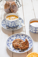 Dates and coconut cookies. Green tea with orange in white and blue cup. White wooden plate. Flatlay.