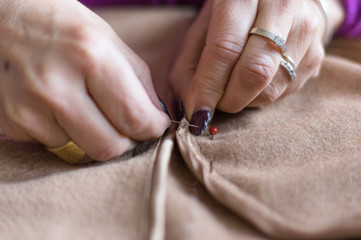 Close up of hands of a seamstress using needle and thread on a cloth