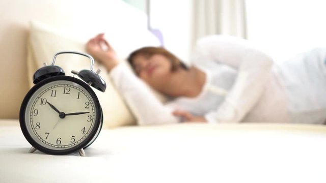 4k focus at young Asian woman sleeping on a white beed then move carmera to focust a vintage alarm clock