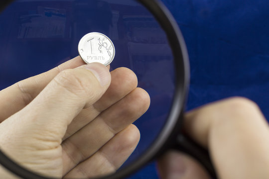 Watching one ruble coin through magnifying glass in the man's fingers on the dark blue background.