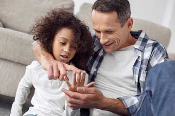 Teaching my daughter. Handsome happy dark-haired man smiling and teaching his daughter to count on her fingers and hugging her