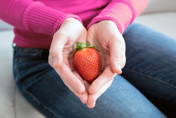 Frau hält behutsam eine frische Erdbeere in der Hand