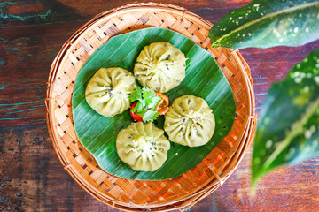 Juicy veggie bun (green dumplings) on a wood plate and on a wooden table. Green matcha boba or bobble tea with organic metal strobe. Chinese food in Bali restaurant. Top view with copy space.
