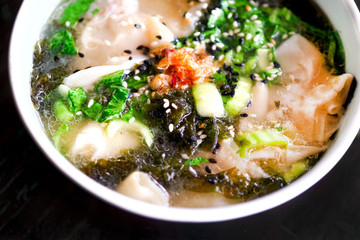 Mushroom chicken Wonton soup on a black plate and on a wooden table. Chinese food. On the table are flowers in a transparent vase and a lilac pot with green leaves. Close-up view with copy space. 