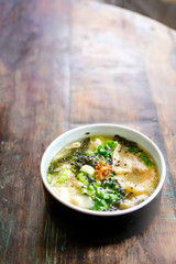 Mushroom chicken Wonton soup on a black plate and on a wooden table. Chinese food. On the table are flowers in a transparent vase and a lilac pot with green leaves. Top view with copy space. 