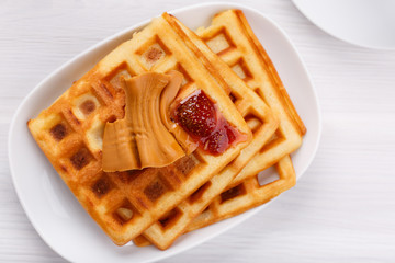 Norwegian brunost on white table. Homemade waffles with Scandinavian brown cheese and strawberry jam.