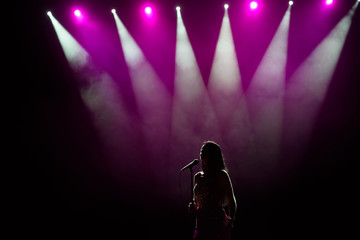 Girl in long gown performing on stage. Girl singing on the stage in front of the lights. Silhouette...