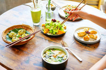 Salmon dumpling salad and Mushroom chicken Wonton soup and chicken kong pao on a white plate and on a wooden table. Chinese food. A female hand with chopsticks takes food. Side view with copy space. 