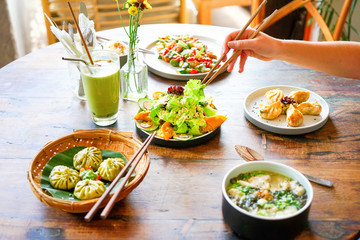 Salmon dumpling salad and Mushroom chicken Wonton soup and chicken kong pao on a white plate and on a wooden table. Chinese food. A female hand with chopsticks takes food. Side view with copy space. 