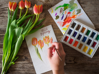 the hand of the artist on the picture with the tulips and the words Hello spring
