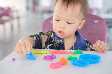 Cute little Asian 18 months old toddler baby boy child having fun playing colorful modeling clay / play dought at play school / child care, Educational toys for kid Creative play for toddlers concept