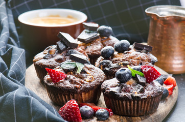 Fresh, blueberry muffins with strawberry, chocolate on a wooden board and stone background with sugar and fruits. Food background. Concept of pastry. 