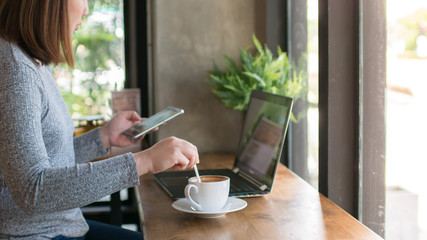 Woman touching and using smartphone with laptop at coffee cafe