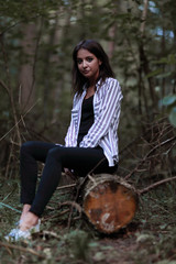 young woman sitting on a log in the woods.