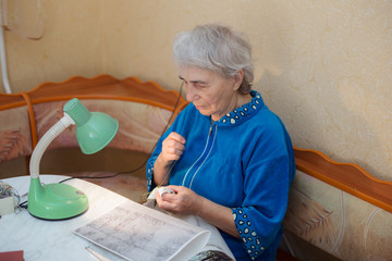 elderly woman is engaged in embroidery